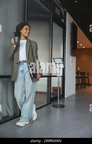 Eine Frau in formeller Kleidung lehnt sich mit einer Tasse Kaffee an ein Geländer Stockfoto