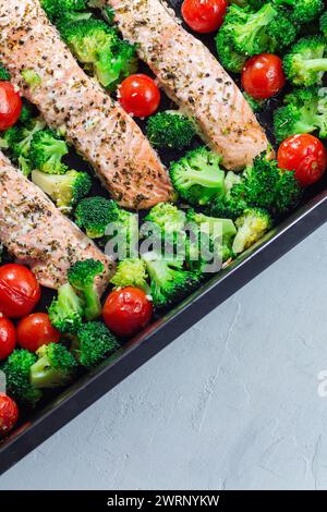 Gebackenes Lachsfilet mit Brokkoli und Tomaten auf einem Bratblech, vertikal, Draufsicht Stockfoto