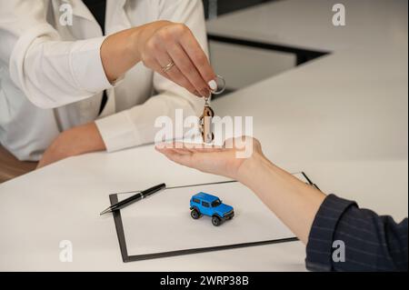 Autokauf-Angebot. Verkäufer übergibt Schlüssel an weibliche Kunden. Stockfoto