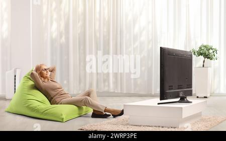 Frau mittleren Alters ruht auf grünem Sitzsack-Sessel vor dem fernseher Stockfoto