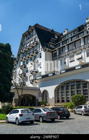 Teilweiser Blick auf den Quitandinha Palace, ein historisches ehemaliges Resort-Hotel mit einigen Autos, die nebeneinander geparkt werden, am Sommernachmittag unter klarem blauem Himmel. Stockfoto