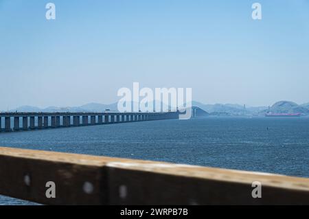 Panoramablick auf die Rio Niteroi Brücke, die über das blaue Wasser der Guanabara Bucht führt, mit Bergsilhouetten in der Ferne unter dem blauen Himmel des Sommernachmittags. Stockfoto