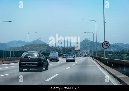 Der Verkehr bewegt sich über die Brückenstraßen des Rio Niteroi, während er in die Stadt Niteroi mit vielen Bergsilhouetten in einer Entfernung unter dem klaren blauen Himmel des Sommers fährt. Stockfoto