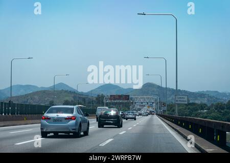 Der Verkehr überquert die Brückenstraßen des Rio Niteroi, während er in die Stadt Niteroi mit vielen Bergsilhouetten in einer Entfernung unter dem klaren blauen Himmel des Sommers fährt. Stockfoto