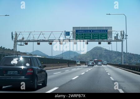 Der Verkehr über die Rio Niteroi-Brückenspuren liegt bei KM 325, während Sie in die Stadt Niteroi mit vielen Bergsilhouetten in der Entfernung unter dem klaren blauen Sommerhimmel fahren. Stockfoto