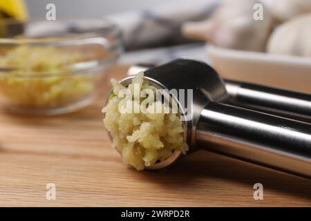 Eine Metallpresse mit zerdrücktem Knoblauch auf Holztisch, Großaufnahme Stockfoto