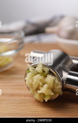 Eine Metallpresse mit zerdrücktem Knoblauch auf Holztisch, Großaufnahme Stockfoto