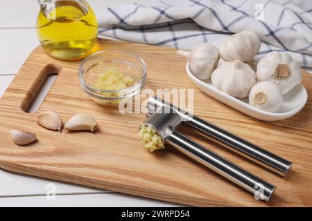 Eine Metallpresse und zerdrückter Knoblauch auf weißem Holztisch, Nahaufnahme Stockfoto