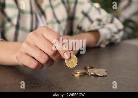 Die arme Frau zählt Münzen an einem grauen Tisch drinnen, Nahaufnahme Stockfoto