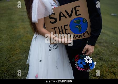 Schöne Jungvermählte küssen sich, während sie ein Schild halten, auf dem steht: RETTEN SIE DIE WELT Stockfoto