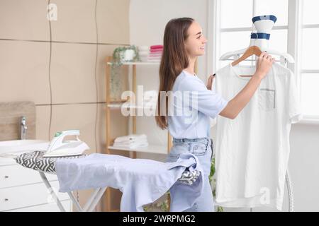 Hübsche junge Frau mit modernem Kleiderdampfer im Waschraum Stockfoto