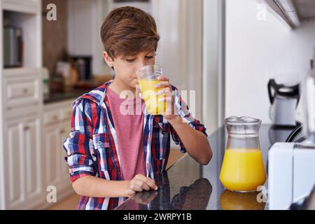 Kinder, Küche und Junge trinken Orangensaft aus Glas am Morgen für Ernährung, Gesundheit oder Ernährung. Frühstück, Tasse und Kinder mit jungen Teenagern Stockfoto