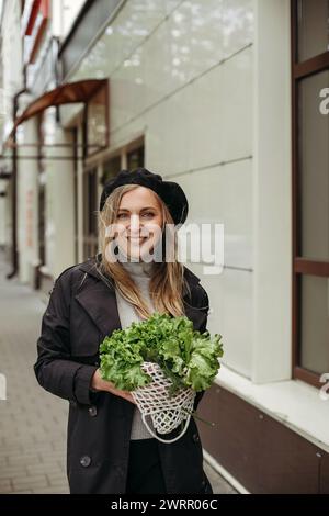 Eine Frau, die steht und einen Haufen Salat vor ihrem Gesicht hält. Vertikales Bild. Stockfoto