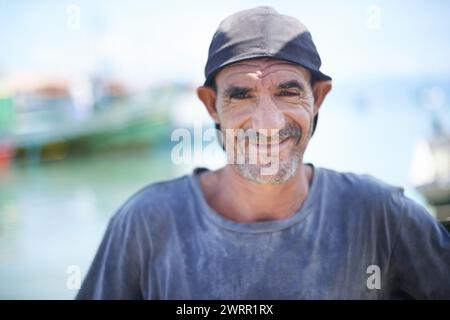 Fischer, Portrait und robuster Mann mit Lächeln, Hafen und Falten durch Sonneneinstrahlung. Boote, Schiffe und Wasser oder Angeln für Arbeit in Brasilien Stockfoto