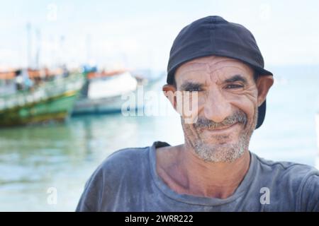 Fischer, Portrait und rauer Mann mit Lächeln, Boote und Fischtrawler im Ozean. Falten, alter und reifer glücklicher Mann aus Brasilien, Nahaufnahme und selbst Stockfoto