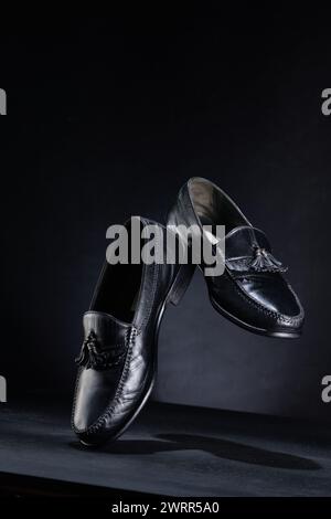 Schwarze Lederschuhe in der Perspektive isoliert auf dunklem Hintergrund mit schwebendem Konzept Stockfoto