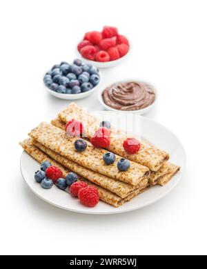 Mit Beeren garnierte Crepes neben kleinen Obstschüsseln und Schokoladenaufstrich. Stockfoto