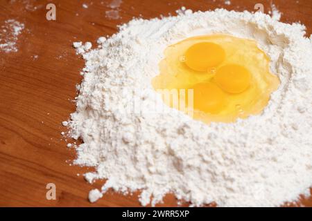 Frische Eier in einem Mehlbrunnen auf einer Holzoberfläche, bereit zum Mischen in Teig Stockfoto