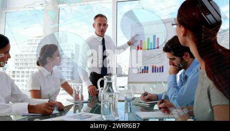 Digitales Composite eines kaukasischen Mannes, der verschiedene Diagramme mit verschiedenen Kollegen in einem Büro diskutiert Stockfoto