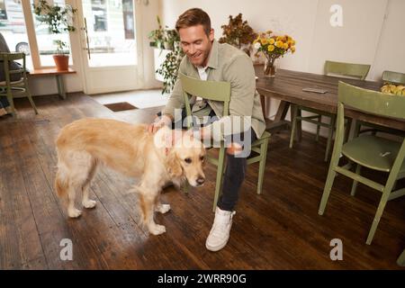 Nahaufnahme Porträt eines hübschen jungen Mannes, der im Café auf seine Bestellung wartet, einen Hund streichelt und sich in einem haustierfreundlichen Café ausruht Stockfoto