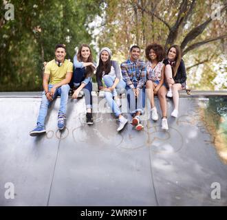 Porträt, Happy und Gruppe von Teenagern im Skatepark in der Stadt, um sich zu verbinden, Spaß zu haben und zusammen zu sitzen. Lächeln, Vielfalt und junge Freunde Stockfoto