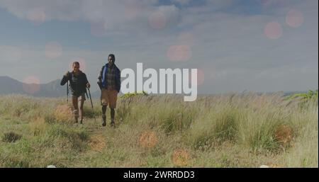 Bild von Lichtflecken über behinderten, birassischen Männern und Frauen, die in Bergen gehen Stockfoto