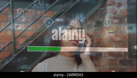 Bild der Daten auf dem digitalen Bildschirm über glückliche, birassische Frau, die im Amt telefoniert Stockfoto