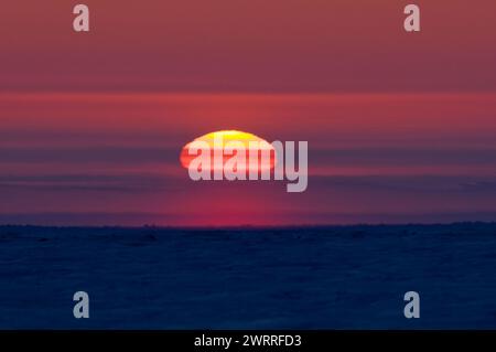 Sonnenuntergang im späten Winter direkt über dem Horizont hinter dem Packeis über dem Beaufort Meer und vor der Küste des arktischen Dorfes Kaktovik Alaska Stockfoto