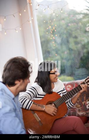 Paare, Frau und spielen Gitarre im Wohnzimmer für Männer, chillen und genießen zusammen auf der Couch. Verheiratet, Frau und Ehemann mit einem Lächeln auf dem Sofa Stockfoto