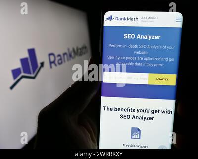 Person, die ein Handy hält, mit Webseite der indischen WordPress SEO-Firma Rank Math vor dem Geschäftslogo. Konzentrieren Sie sich auf die Mitte des Telefondisplays. Stockfoto