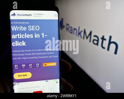 Person, die ein Smartphone hält, mit Webseite des indischen WordPress SEO-Unternehmens Rank Math vor dem Geschäftslogo. Konzentrieren Sie sich auf die Mitte des Telefondisplays. Stockfoto
