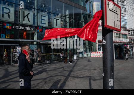 05.03.2024, Berlin, Deutschland, Europa - Straßenszene zeigt einen Mann mit Zigarette und rotem Handy neben einer roten Plastikfolie, die in den Wind bläst. Stockfoto