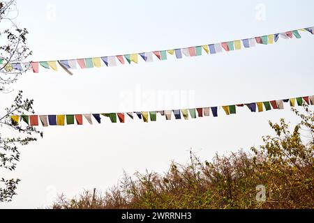 Farbenfrohe tibetische Gebetsfahnen flattern alte Gebete in einen ruhigen Bergwind auf der Spitze eines hohen Hügels auf blauem Himmel und symbolisieren spirituelles ener Stockfoto