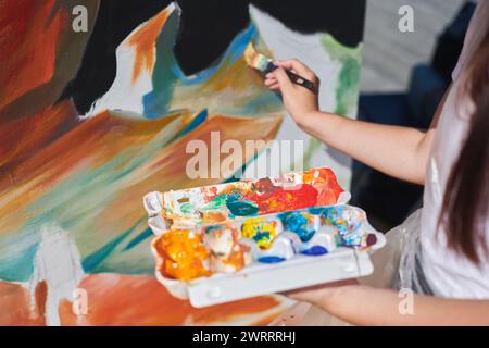 Weibliche Malerhand malt leidenschaftlich mit Pinsel für die Straßenausstellung im Freien mit leuchtenden Farben, Nahaufnahme Stockfoto