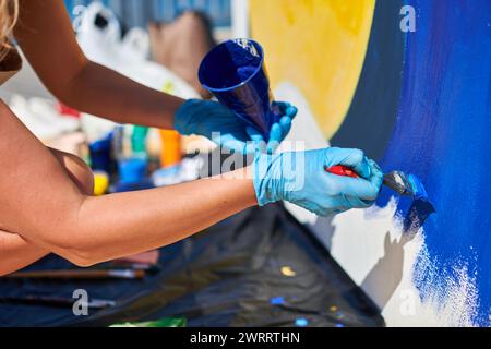 Weibliche Malerhand malt leidenschaftlich mit Pinsel für die Straßenausstellung im Freien mit leuchtenden Farben, Nahaufnahme Stockfoto