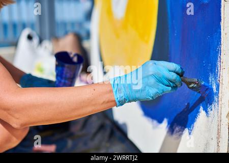 Weibliche Malerhand malt leidenschaftlich mit Pinsel für die Straßenausstellung im Freien mit leuchtenden Farben, Nahaufnahme Stockfoto