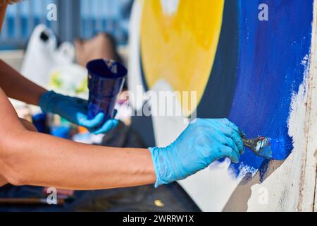 Weibliche Malerhand malt leidenschaftlich mit Pinsel für die Straßenausstellung im Freien mit leuchtenden Farben, Nahaufnahme Stockfoto