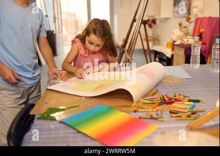 Talentiertes, inspiriertes Schulmädchen im Grundalter in rosa Kleid, Malerei in der Schule für kreative Kunst. Junge und Mädchen lernen Zeichnen mit Pastellfarben während der Besichtigung Stockfoto