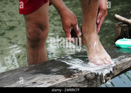 Asiatischer Mann, der im traditionellen Fluss badete und die Füße mit Seife putzte. Stockfoto