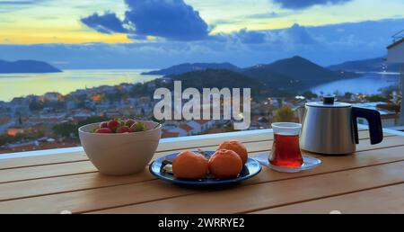 Romantische Teeparty bei Sonnenuntergang für Paare. Frische Erdbeeren und Mandarinen, schwarzer Tee in türkischer Tasse. Niemand, Terrasse mit Blick auf die Stadt am Meer Stockfoto