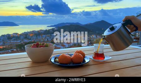 Romantische Teeparty bei Sonnenuntergang für Paare. Frische Erdbeeren und Mandarinen, schwarzer Tee in türkischer Tasse. Terrasse mit Blick auf die Stadt am Meer Stockfoto