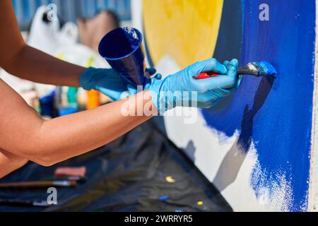 Weibliche Malerhand malt leidenschaftlich mit Pinsel für die Straßenausstellung im Freien mit leuchtenden Farben, Nahaufnahme Stockfoto