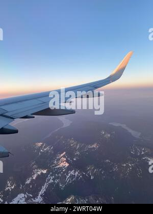 Der Sonnenaufgang über den schneebedeckten felsigen Bergen, von oben gesehen, während Sie nach Hause fliegen Stockfoto