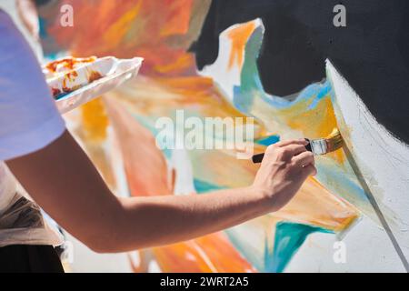 Weibliche Malerhand malt leidenschaftlich mit Pinsel für die Straßenausstellung im Freien mit leuchtenden Farben, Nahaufnahme Stockfoto
