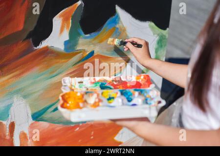 Weibliche Malerhand malt leidenschaftlich mit Pinsel für die Straßenausstellung im Freien mit leuchtenden Farben, Nahaufnahme Stockfoto