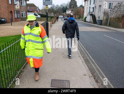 Die Lutscher-Dame in einem farbenfrohen Hiviz-Hut und Mantel geht zu ihrer Arbeit und hilft Schülern, die Straße sicher zu überqueren. Stockfoto