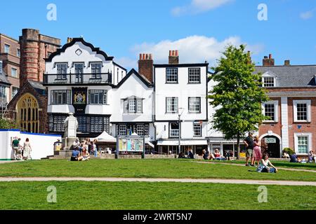 Vorderansicht der Mols und anderer Gebäude in der Kathedrale nahe Touristen, die die Sonne genießen, Exeter, Devon, Großbritannien, Europa. Stockfoto