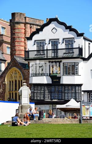 Vorderansicht des Mols-Gebäudes in der Kathedrale in der Nähe mit einer Statue von Richard Hooker im Vordergrund und Touristen, die die Sonne genießen, Exeter, Großbritannien. Stockfoto