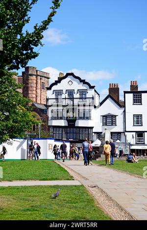 Vorderansicht der Mols und anderer Gebäude in der Kathedrale nahe Touristen, die die Sonne genießen, Exeter, Devon, Großbritannien, Europa. Stockfoto