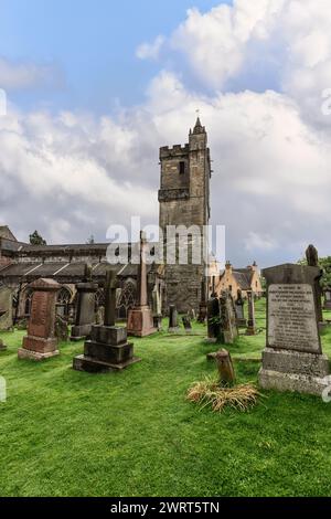 Vertikaler Blick auf die Kirche des Heiligen, unhöflichen antiken Turms, Wache über den verwitterten Grabsteinen auf dem historischen Friedhof. Stirling Stockfoto